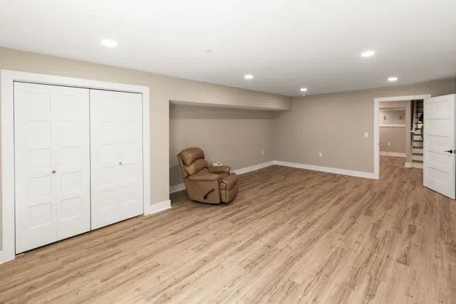 Finished basement with wood-look flooring, recessed lights, white double doors and a brown recliner.