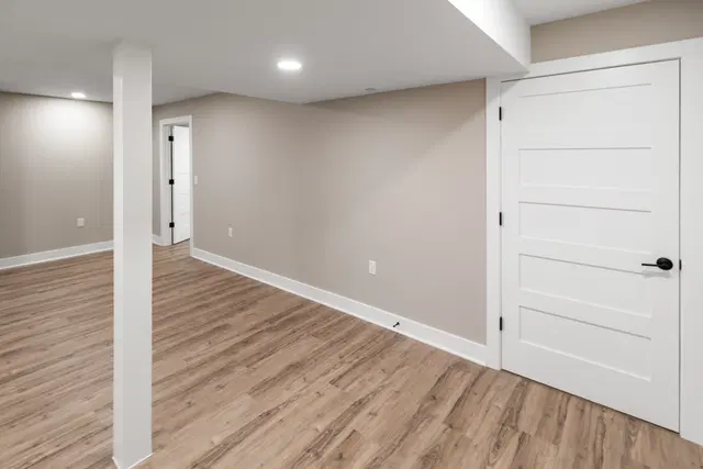 White paneled basement door beside a wood-look floor, gray walls and a narrow white support column.