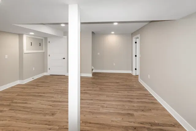 Wide basement view with wood-look flooring, a central white support post and open doorways between areas.