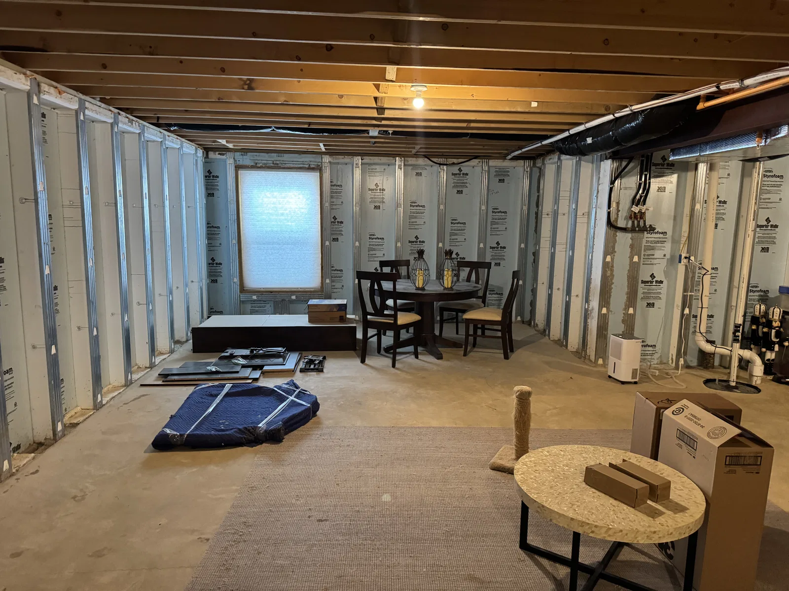 Before finishing: basement with a concrete floor, exposed ceiling joists, insulated walls and a dining table near the window.