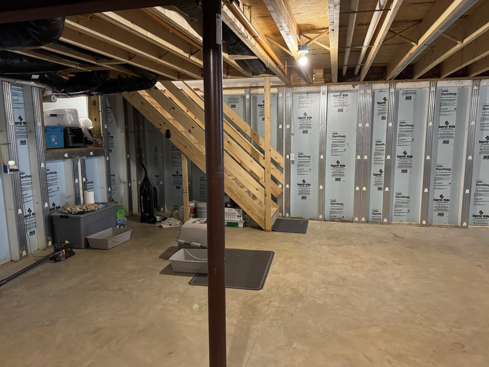 Before finishing: open wooden basement staircase, insulated wall framing and steel support post above a concrete floor.