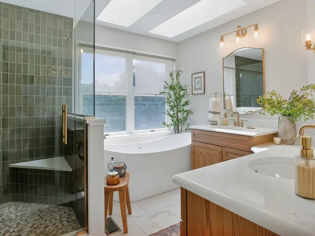 Bathroom with a green-tiled glass shower, freestanding tub, wood vanities and gold-tone fixtures.