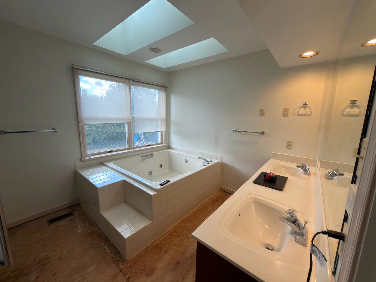 Before remodeling: built-in jetted bathtub beneath two skylights and a window, beside a double-sink vanity.