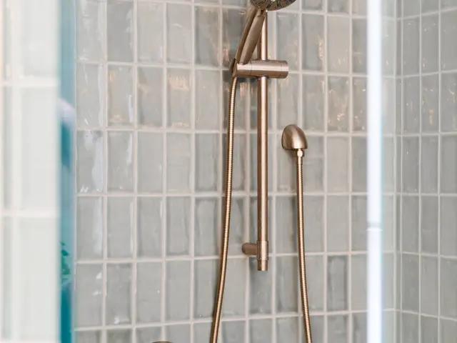 Gold-tone shower riser, handheld spray and controls mounted on green tile.