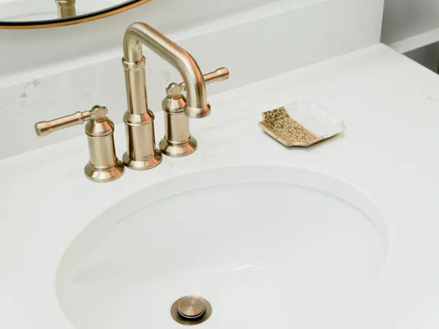 White bathroom sink with a gold-tone faucet, cross handles and a small soap dish.