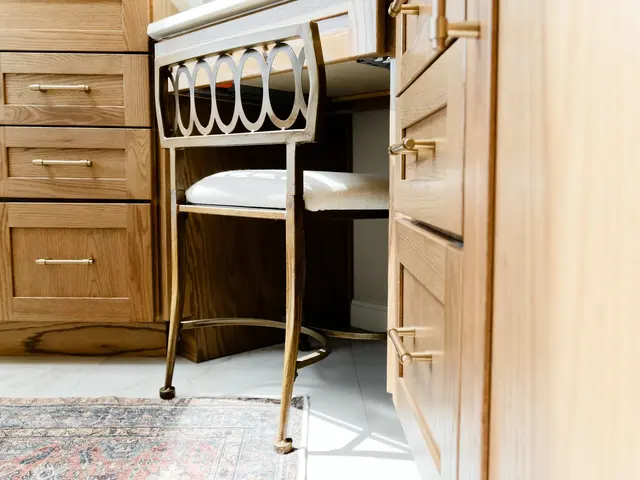 Bathroom makeup chair tucked between wood vanity cabinets beneath a white countertop.