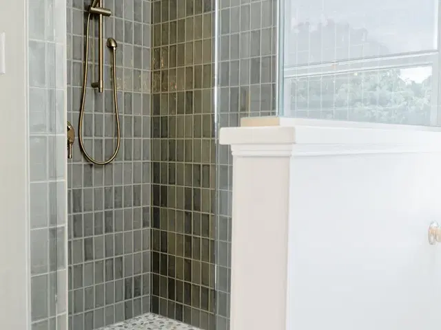Green-tiled shower and glass half-wall beside a freestanding tub beneath the window.