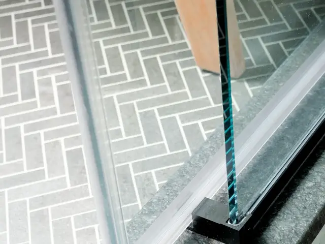 Dark shower door frame meeting herringbone floor tile at the threshold.