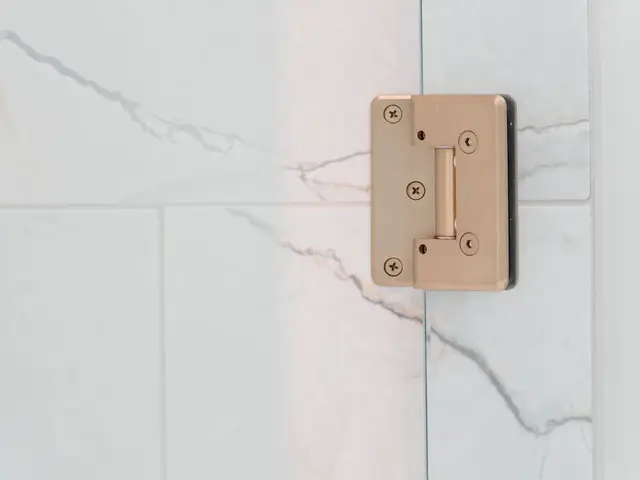 Detail of a gold-tone glass shower hinge against marble-look wall tile.