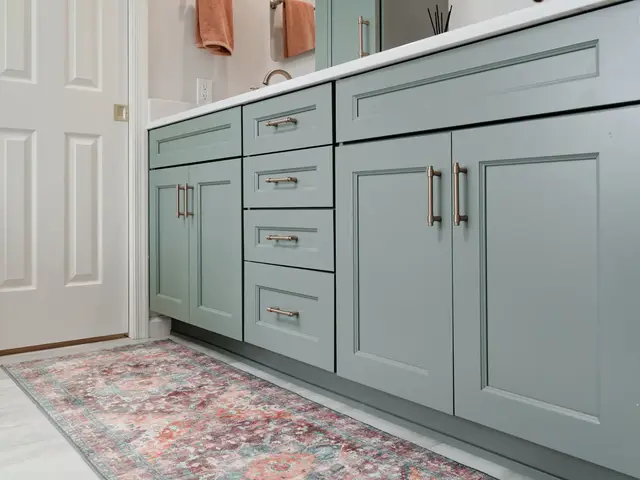 Low view of blue-green vanity cabinetry with gold-tone pulls above a colorful runner.