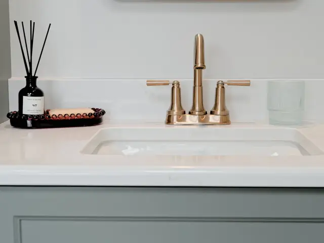 White vanity sink with a gold-tone faucet above blue-green cabinets.