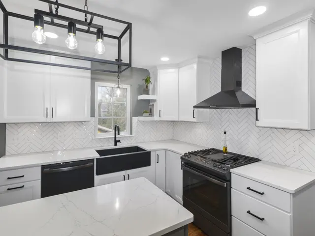 Kitchen cooking and sink areas with a white herringbone tile backsplash, black vent hood, white cabinets and an open-frame pendant light.