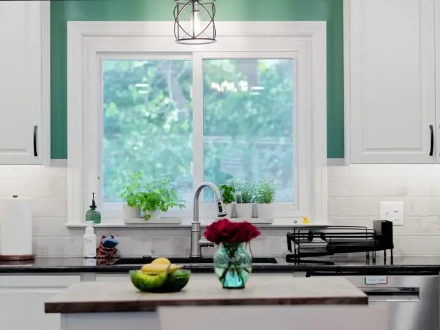 White kitchen cabinetry and dark countertops around a stainless sink beneath a window framed by green walls.