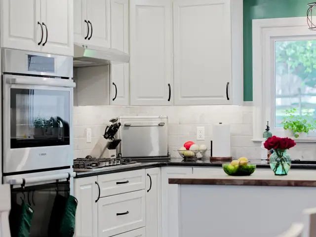 Kitchen cooking area with stacked stainless wall ovens, white cabinets, a gas cooktop and a wood-topped island.