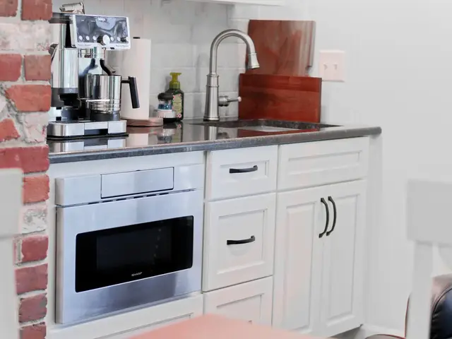 Coffee counter beside the brick fireplace with a small stainless sink, white cabinets and a built-in beverage refrigerator.
