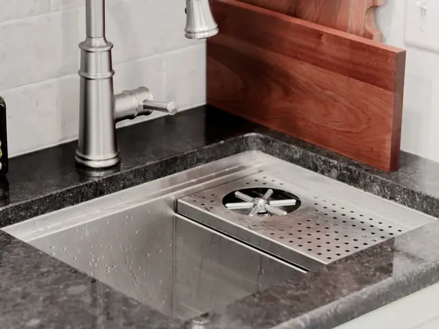 Small stainless sink and arched faucet set into the dark coffee-area countertop beneath wooden cutting boards.