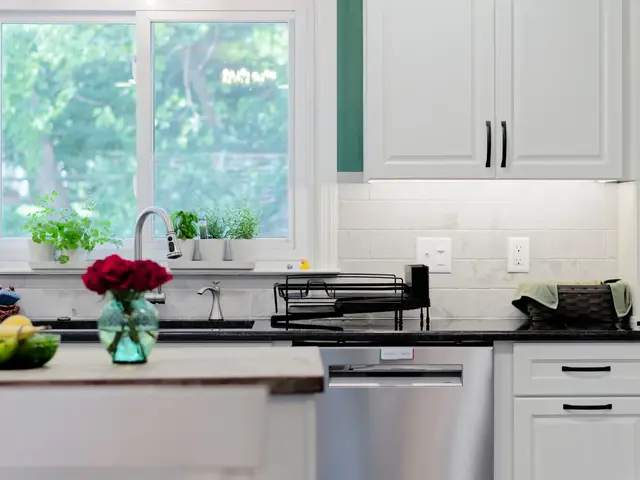 View across the wood-topped island toward the sink wall, white cabinetry, dark countertops and green-framed kitchen window.
