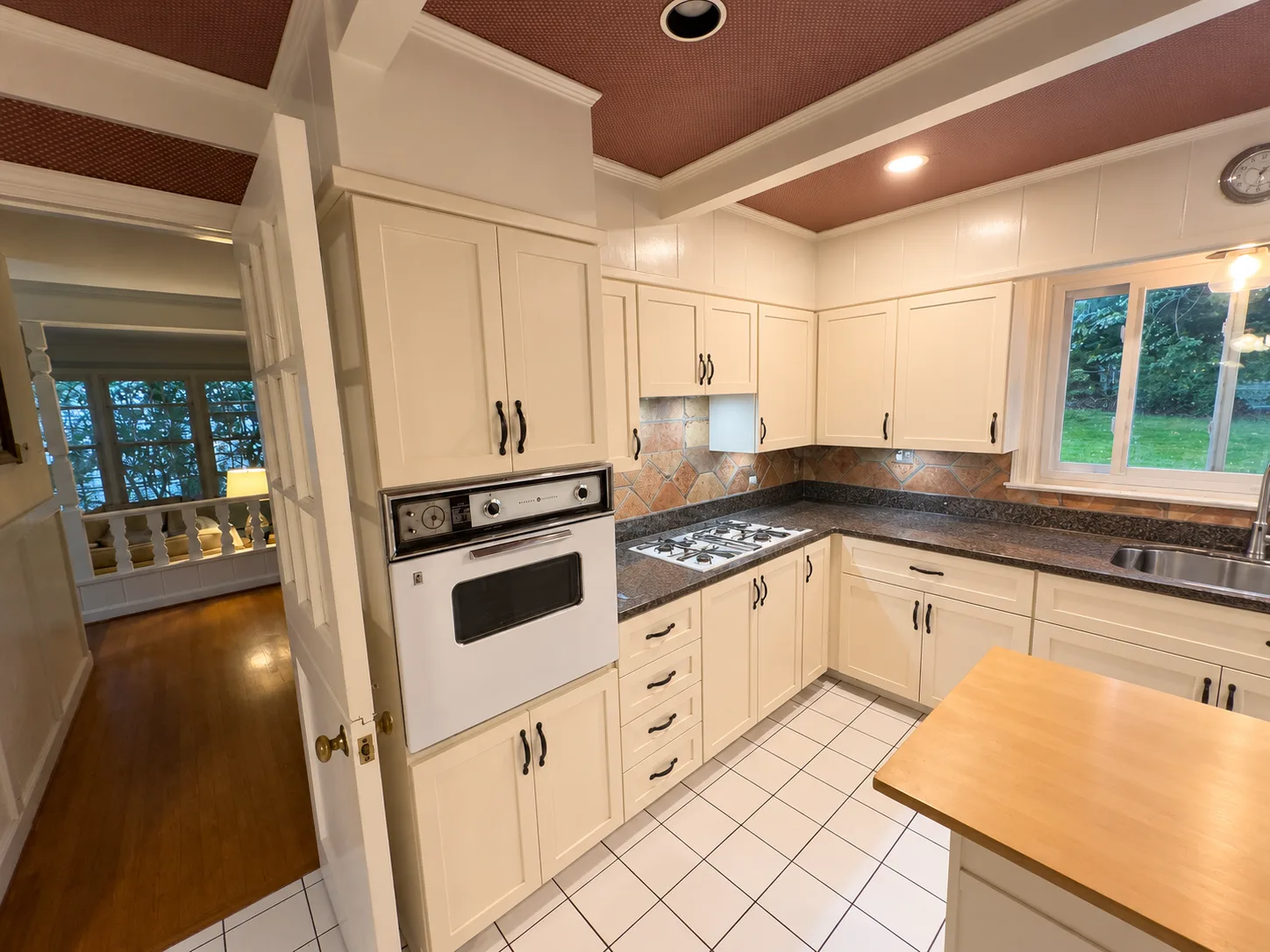 Before remodeling: Harrisburg kitchen with white cabinets, a white wall oven and gas cooktop, diagonal tile backsplash, white floor tile and a brown beamed ceiling.