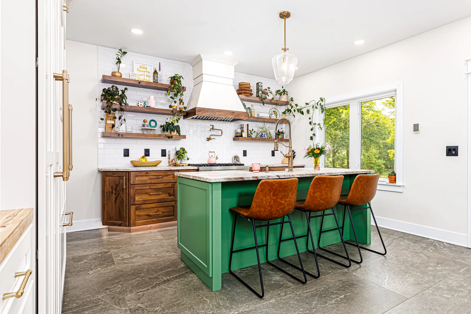 Finished kitchen overview with a green island, three woven stools, wood base cabinets, white tall cabinetry and floating shelves.