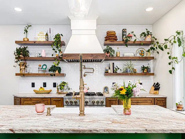 View across the island countertop and tall faucet toward a white range hood, wood shelving and cooking area.