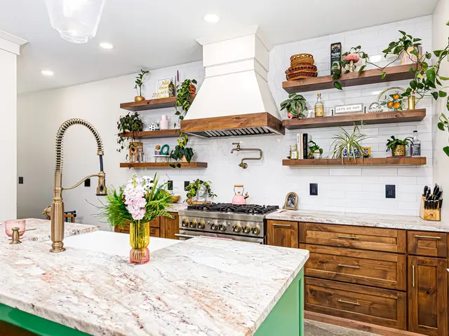 Angled view of the kitchen island, wood cabinets, range hood and floating shelves with trailing plants.