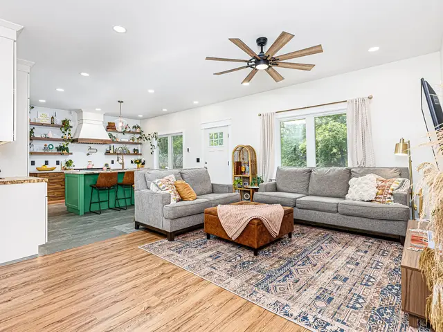 Open kitchen and adjoining living room with a gray sectional, patterned rug and wood flooring.